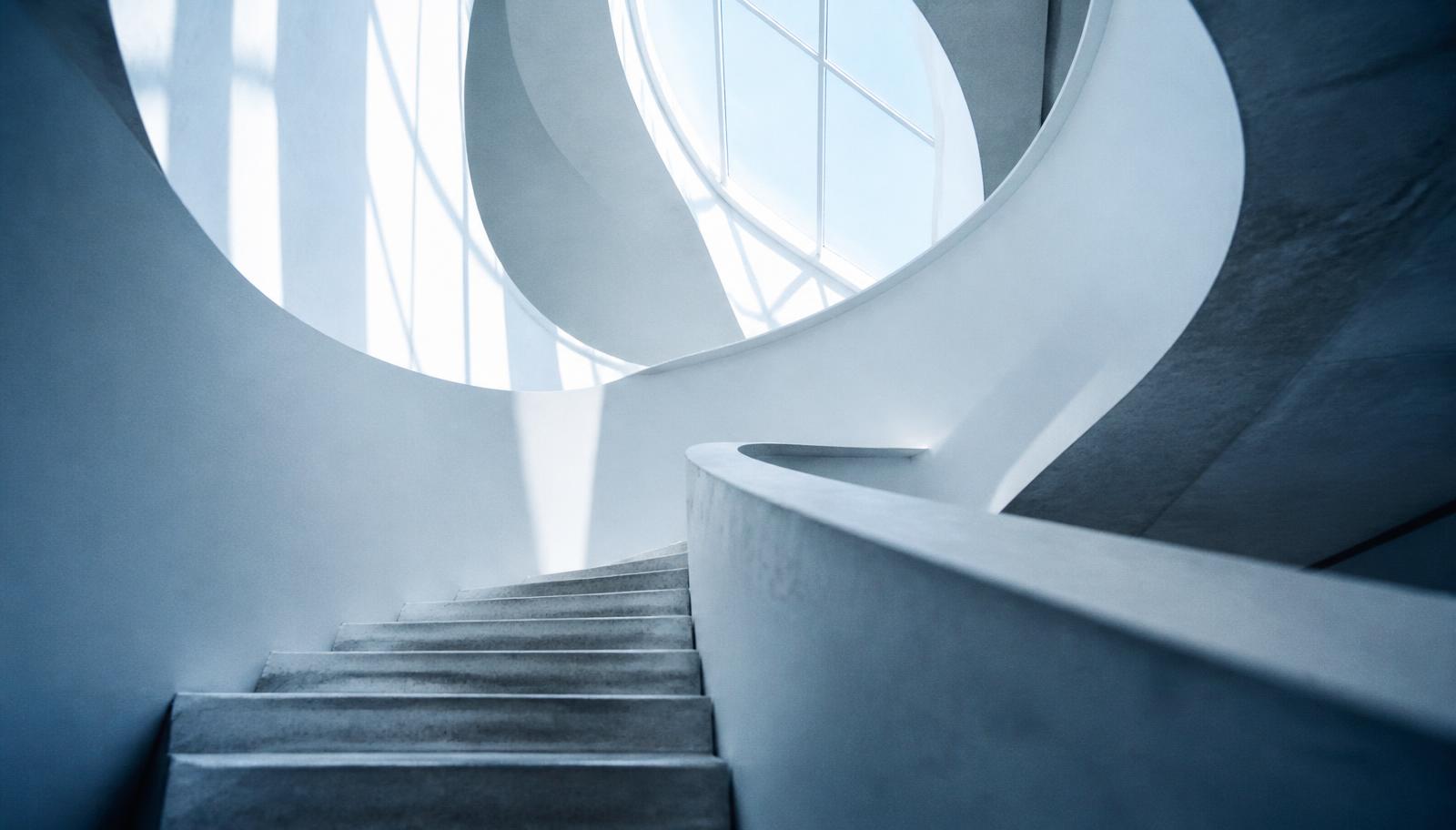 A pale concrete stairwell rising through cool morning daylight